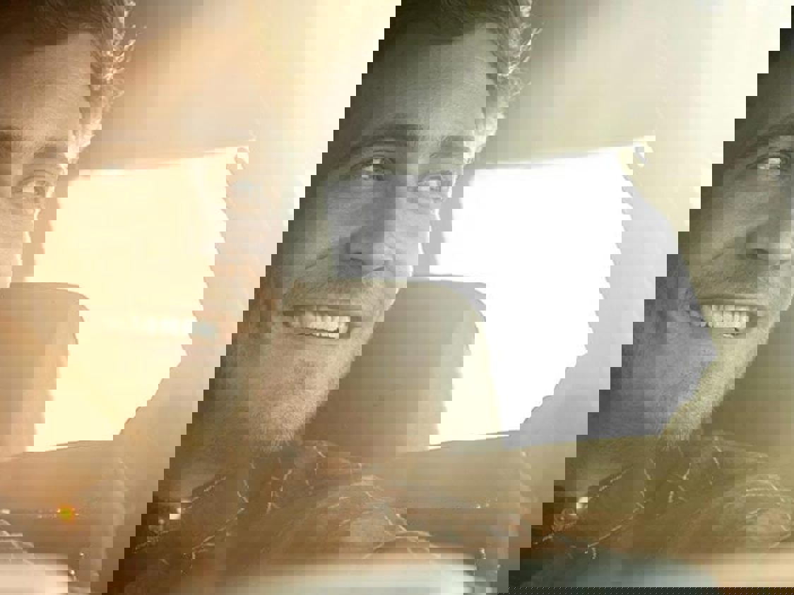 En mand sidder i en bil og smile mens solen skinner ind gennem bagruden.