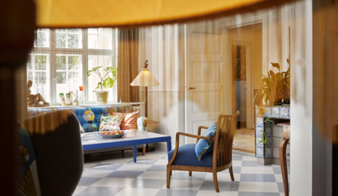 Ett stilfullt vardagsrum med trämöbler, färgglada kuddar på blå soffa och schackrutigt golv i ljus miljö.