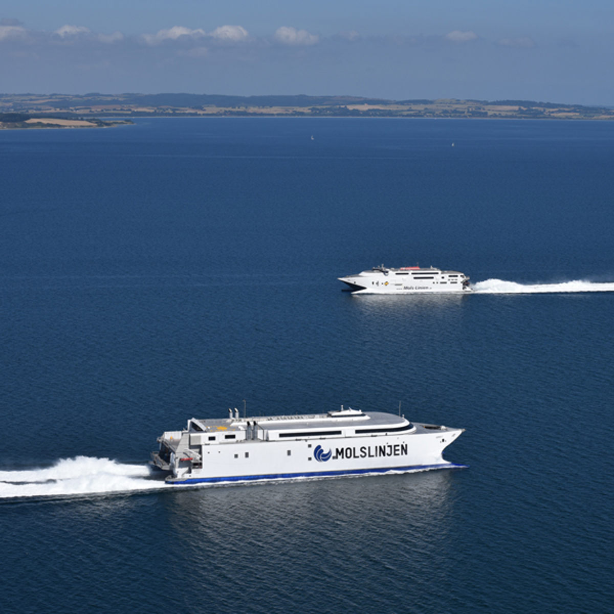 Molslinjen færger sejler i åbent hav med roligt vand og klar himmel i baggrunden.
