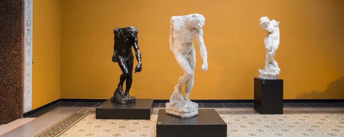 Tre skulpturer på Glyptoteket mot en gul bakgrund, två vita och en mörk, stående på svarta socklar.