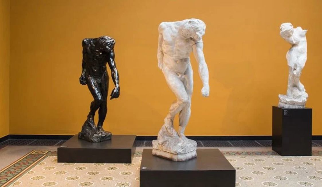 Tre skulpturer på Glyptoteket mot en gul bakgrund, två vita och en mörk, stående på svarta socklar.