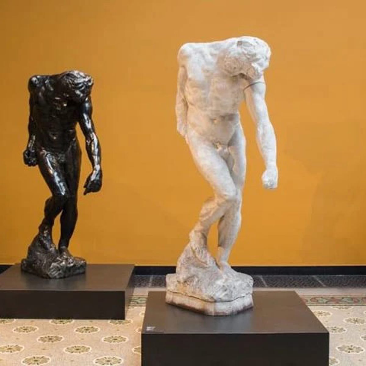 Tre skulpturer på Glyptoteket mot en gul bakgrund, två vita och en mörk, stående på svarta socklar.