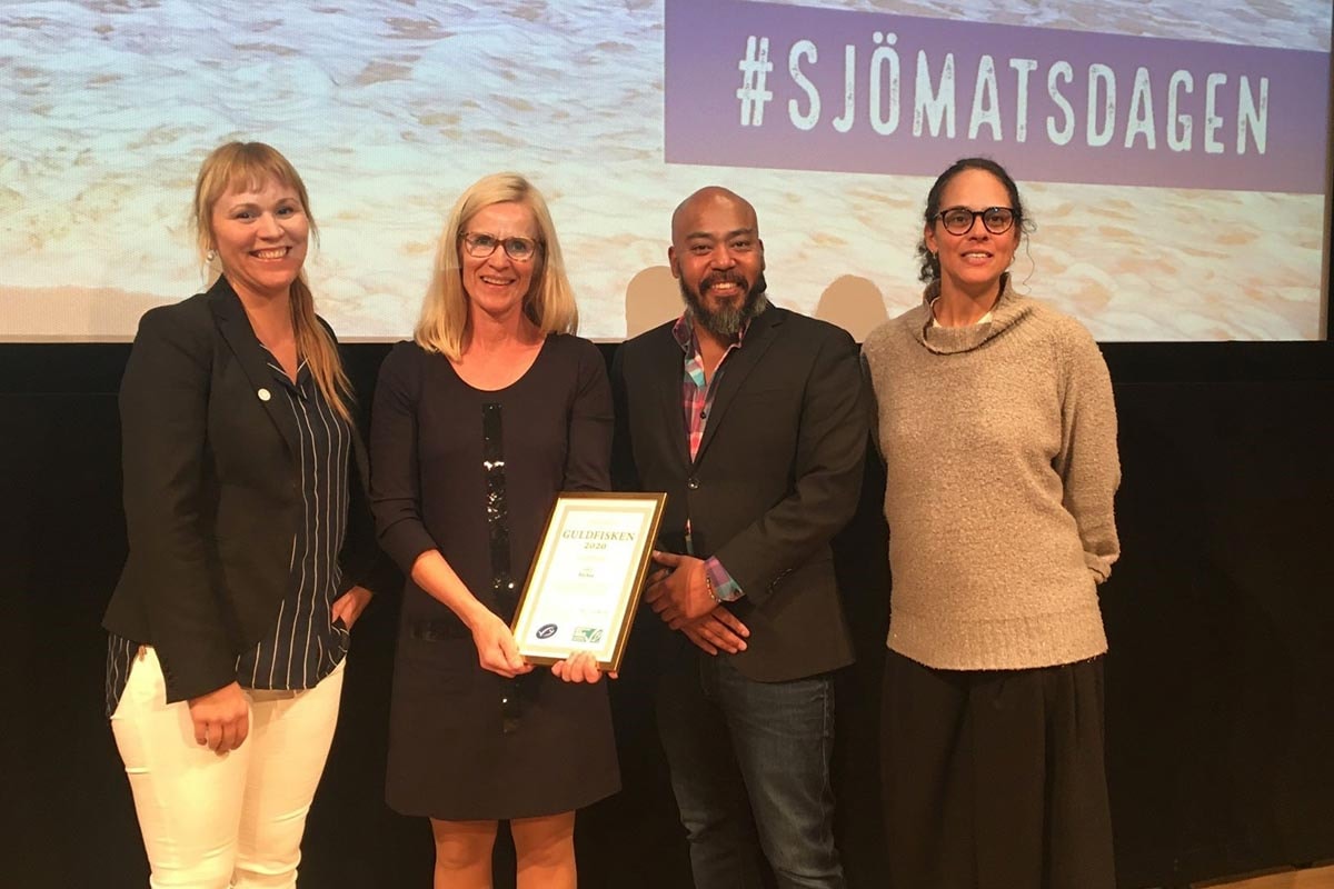 Fyra personer står på scenen med händerna framför sig och håller i ett pris.