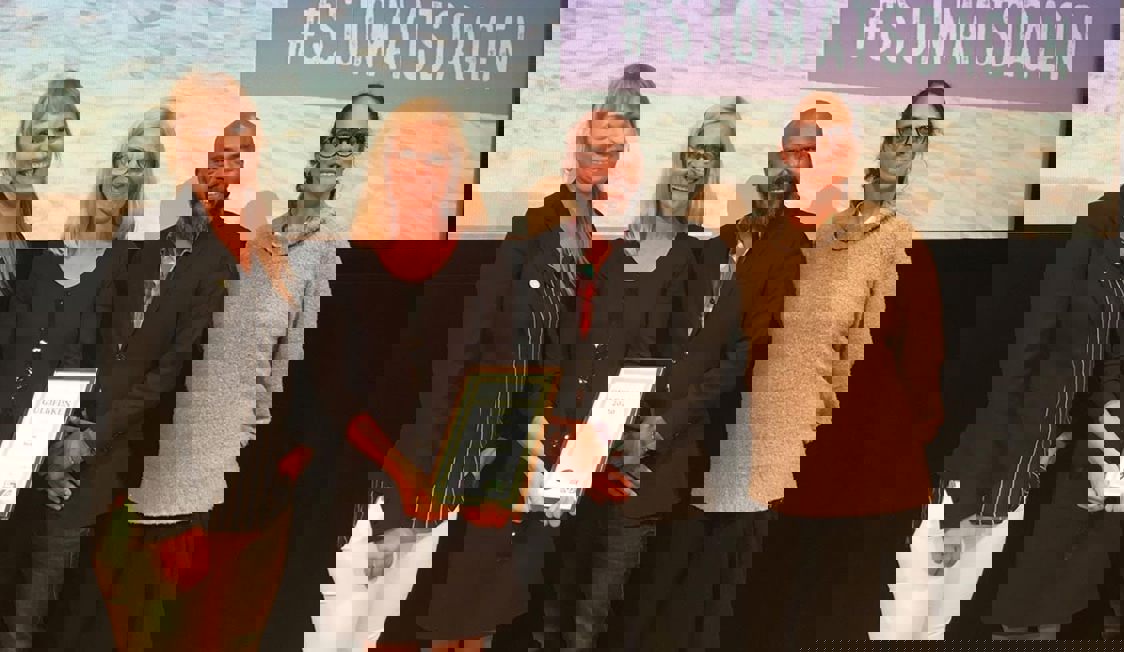 Fyra personer står på scenen med händerna framför sig och håller i ett pris.