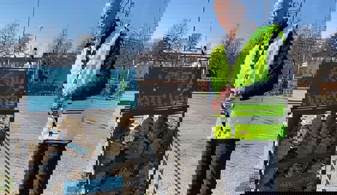 Insektshotel i træ ses til venstre for en mand i gul sikkerhedsvest.