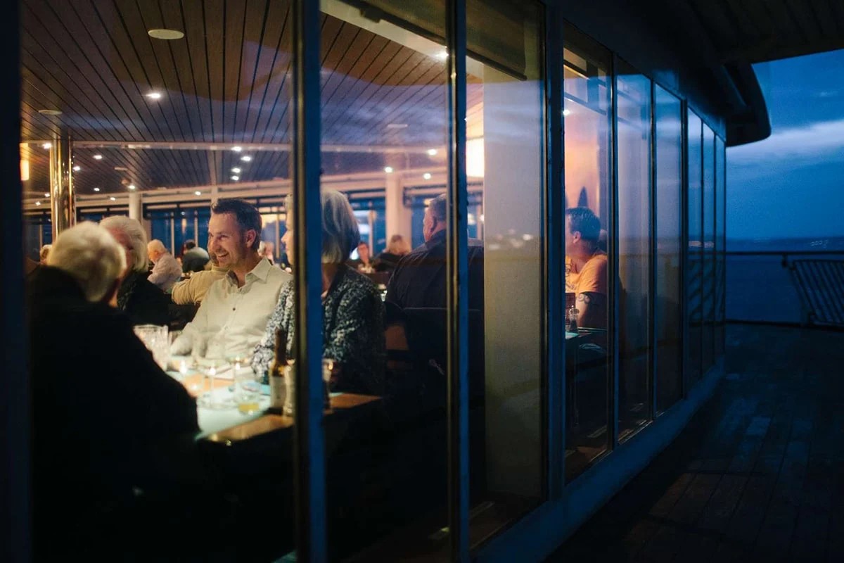 Middag på däck med människor som njuter av ett julbord ombord i kvällsljus.