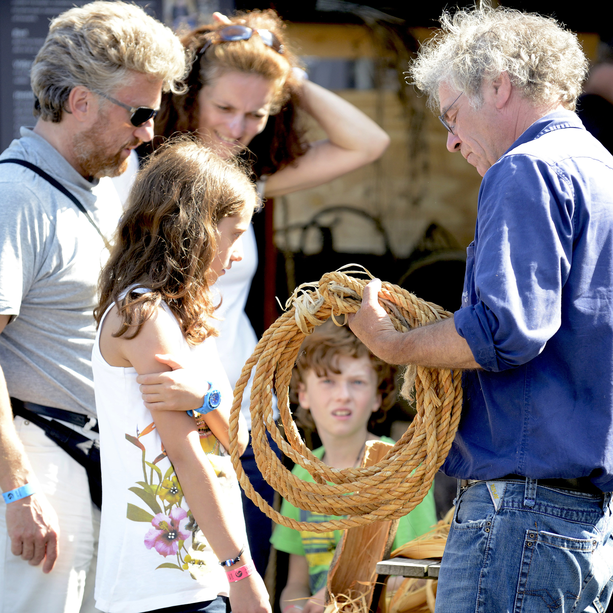 Mand viser en gruppe børn, hvordan man arbejder med reb i en udendørs snorretrækningsdemonstration.