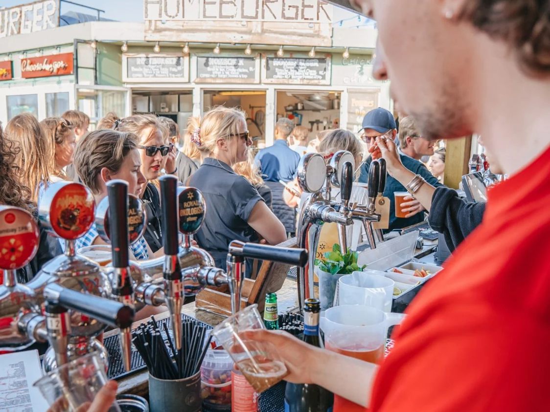 Barpersonal serverar dryck på Reffen Vibes-konsert medan människor samlas runt bardisken.