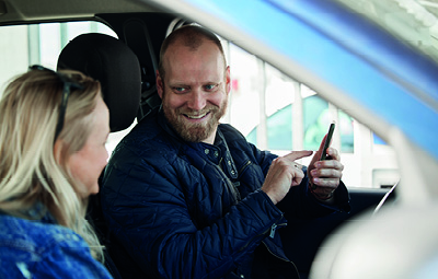 Man using MobilePay app in a car while smiling at a woman in the passenger seat.