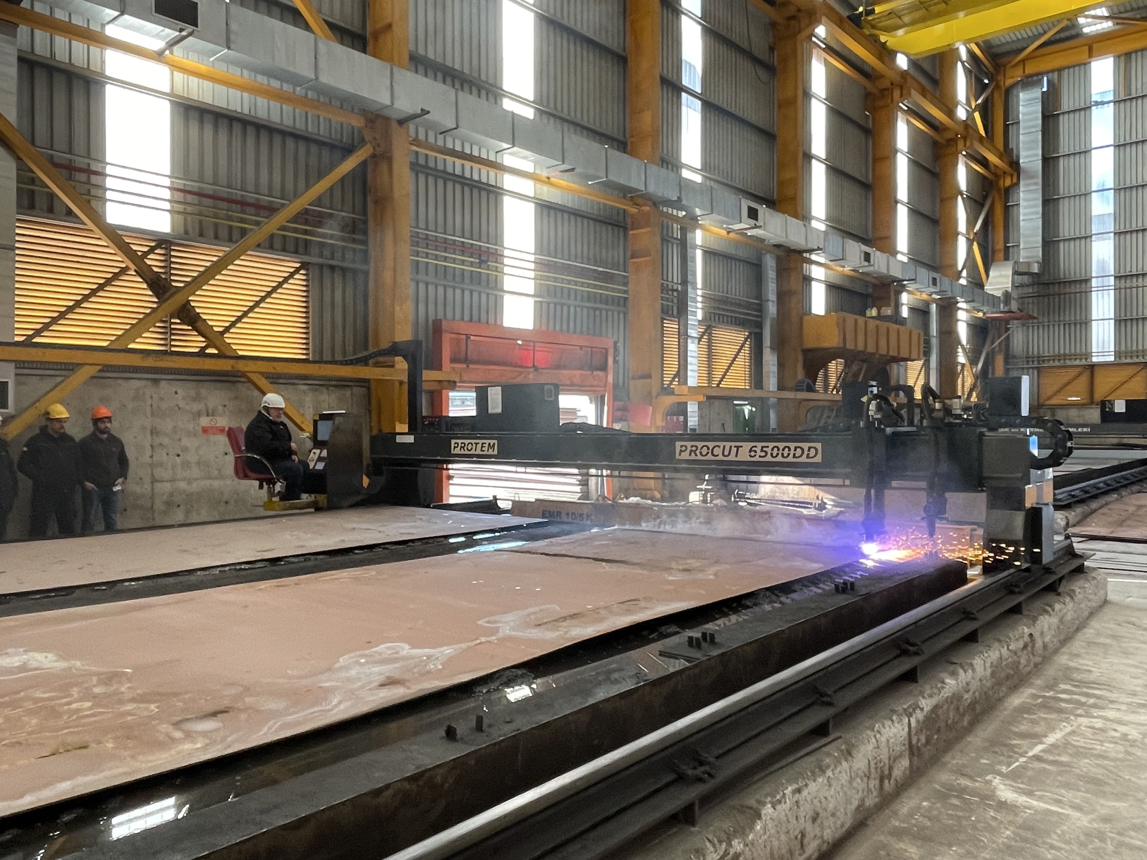 Industrial CNC maskine Protem ProCut 6500DD skærer metalplader i moderne fabrikshal med gnister og lys.