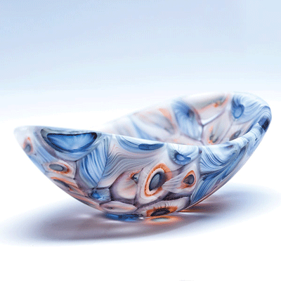 Håndlavet glasfad i blå og orange mønster på hvid baggrund, set fra skråt ovenfra.