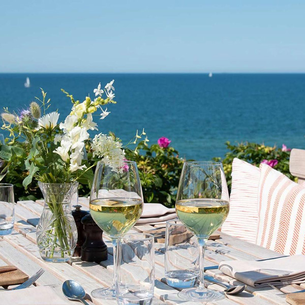 Sommar Dukat dukning med glas och blommor på ett bord vid havet en solig dag.