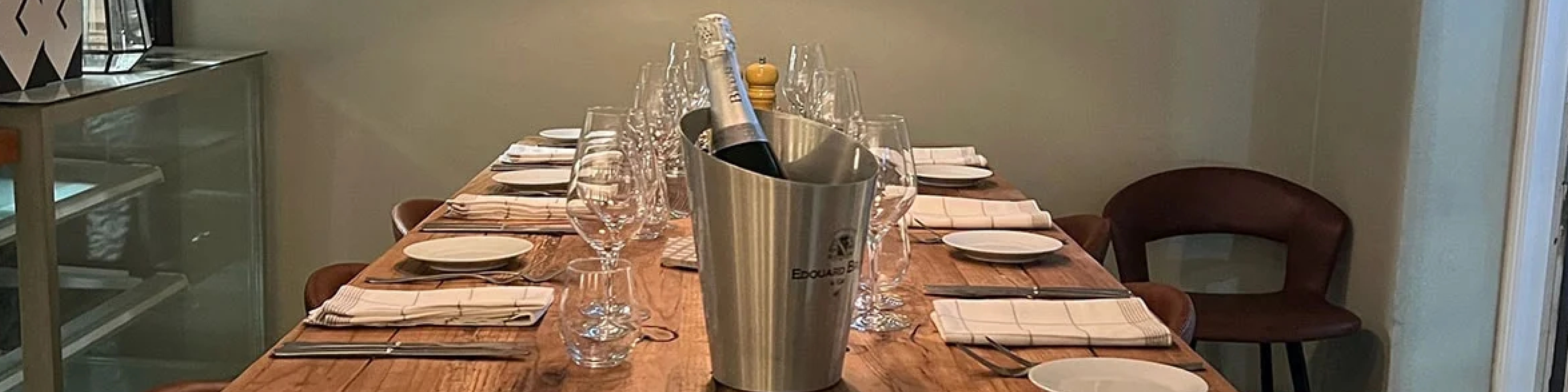 Elegant dukning med Banner champagnekylare på träbord, omgiven av vinglas och tallrikar.