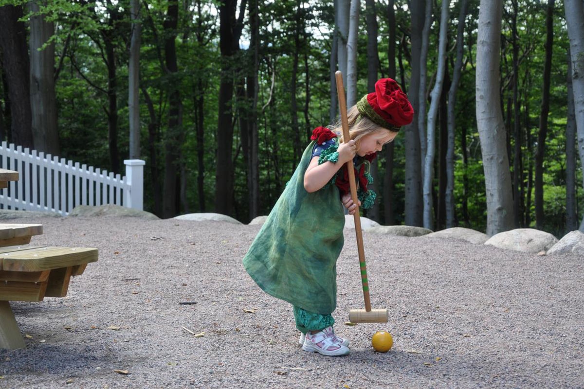 Et barn spillet cricket med træer og skov i baggrunden.