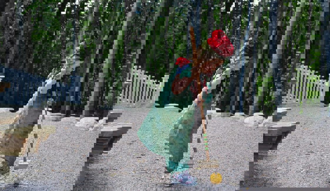 Et barn spillet cricket med træer og skov i baggrunden.