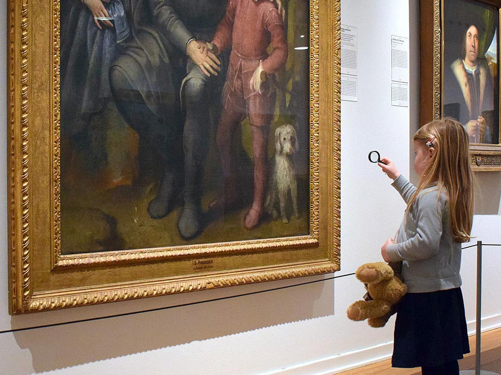 En flicka med förstoringsglas studerar en stor tavla på ett konstmuseum.