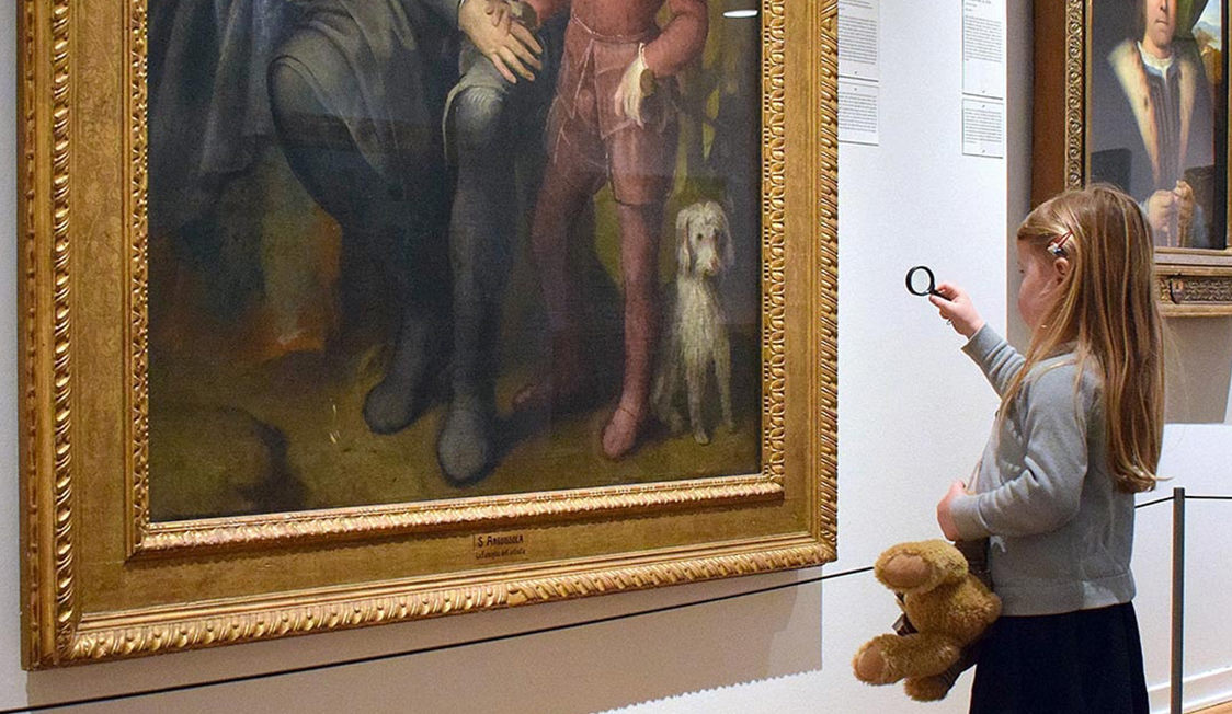 En flicka med förstoringsglas studerar en stor tavla på ett konstmuseum.