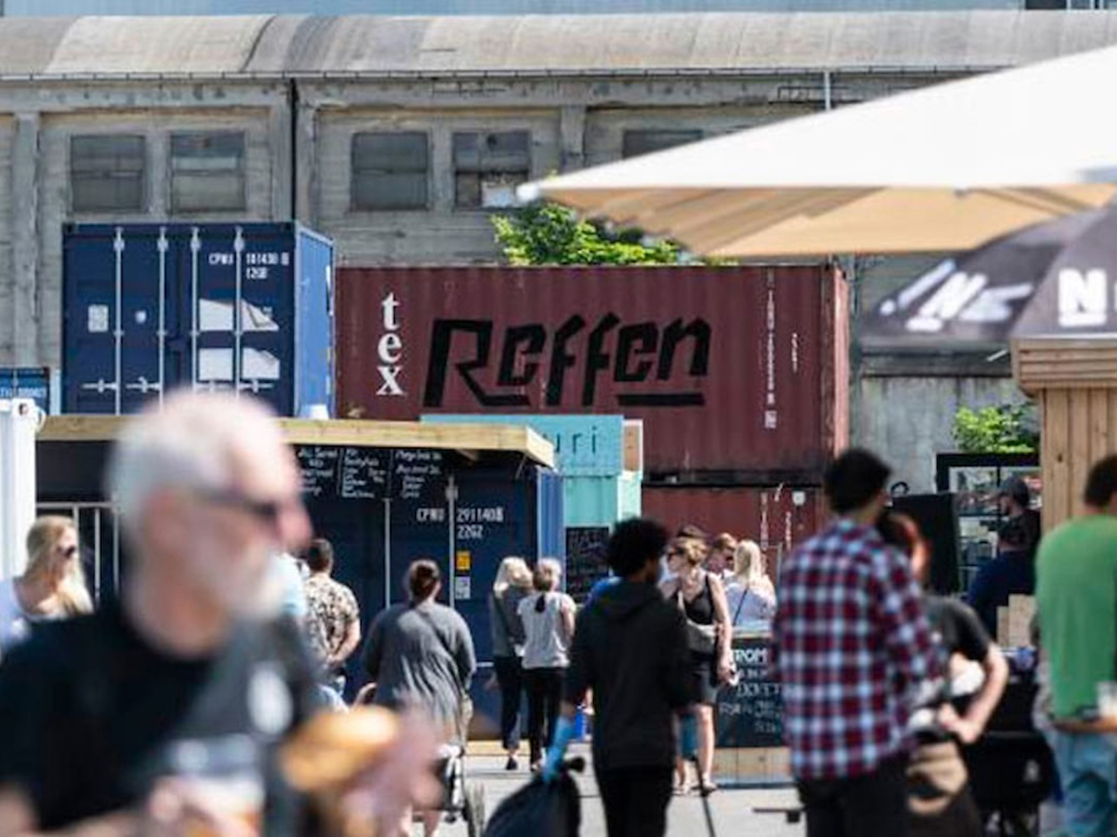 Folktät Refshaleøen med containrar och människor som njuter av en livlig marknad i solen.