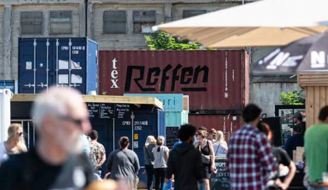 Folktät Refshaleøen med containrar och människor som njuter av en livlig marknad i solen.