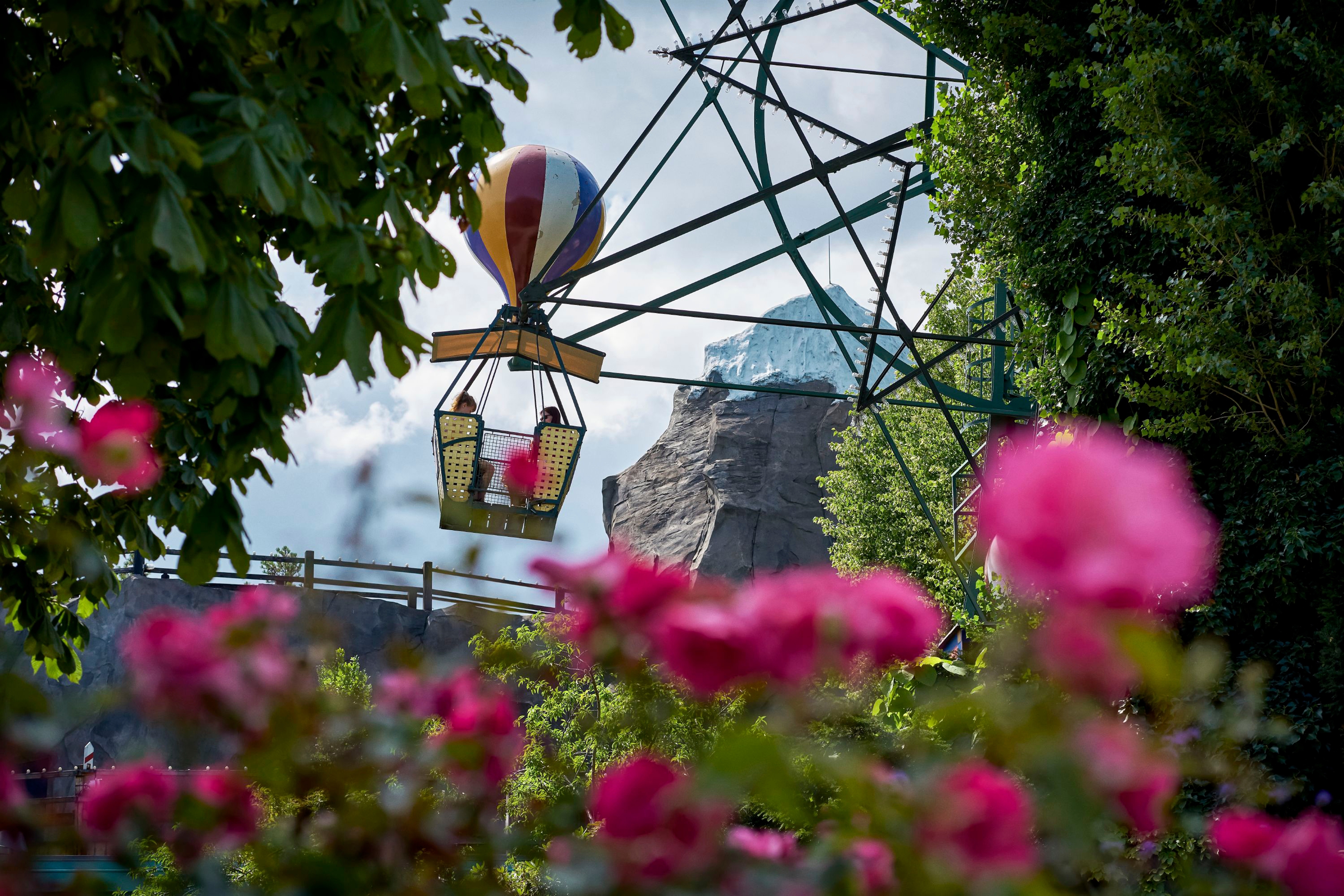 Varmluftballon-forlystelse svæver over blomstrende roser i en forlystelsespark på en solrig dag.
