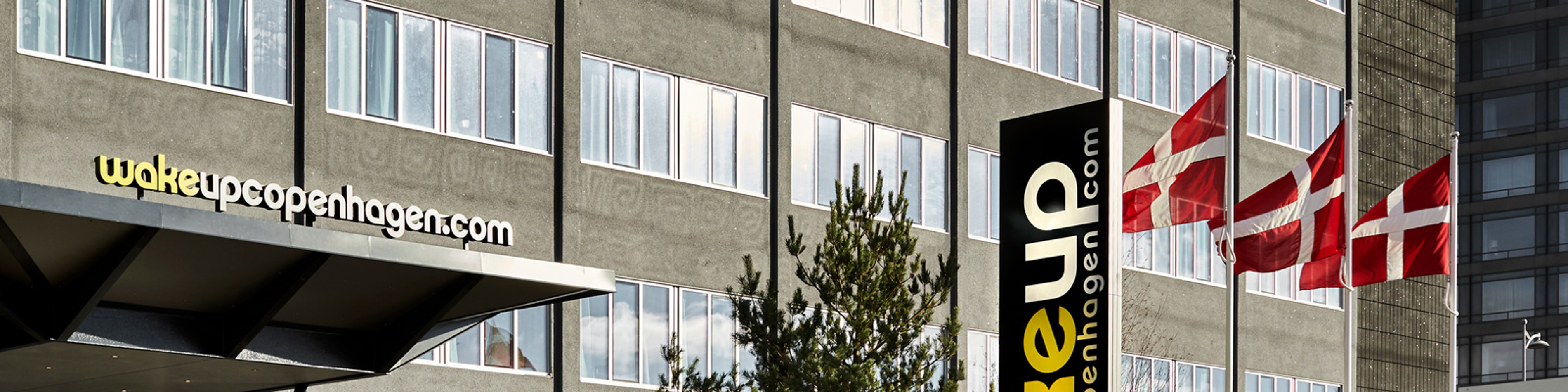Wakeup Copenhagen hotel med danske flag foran bygningen og moderne arkitektur i dagslys.