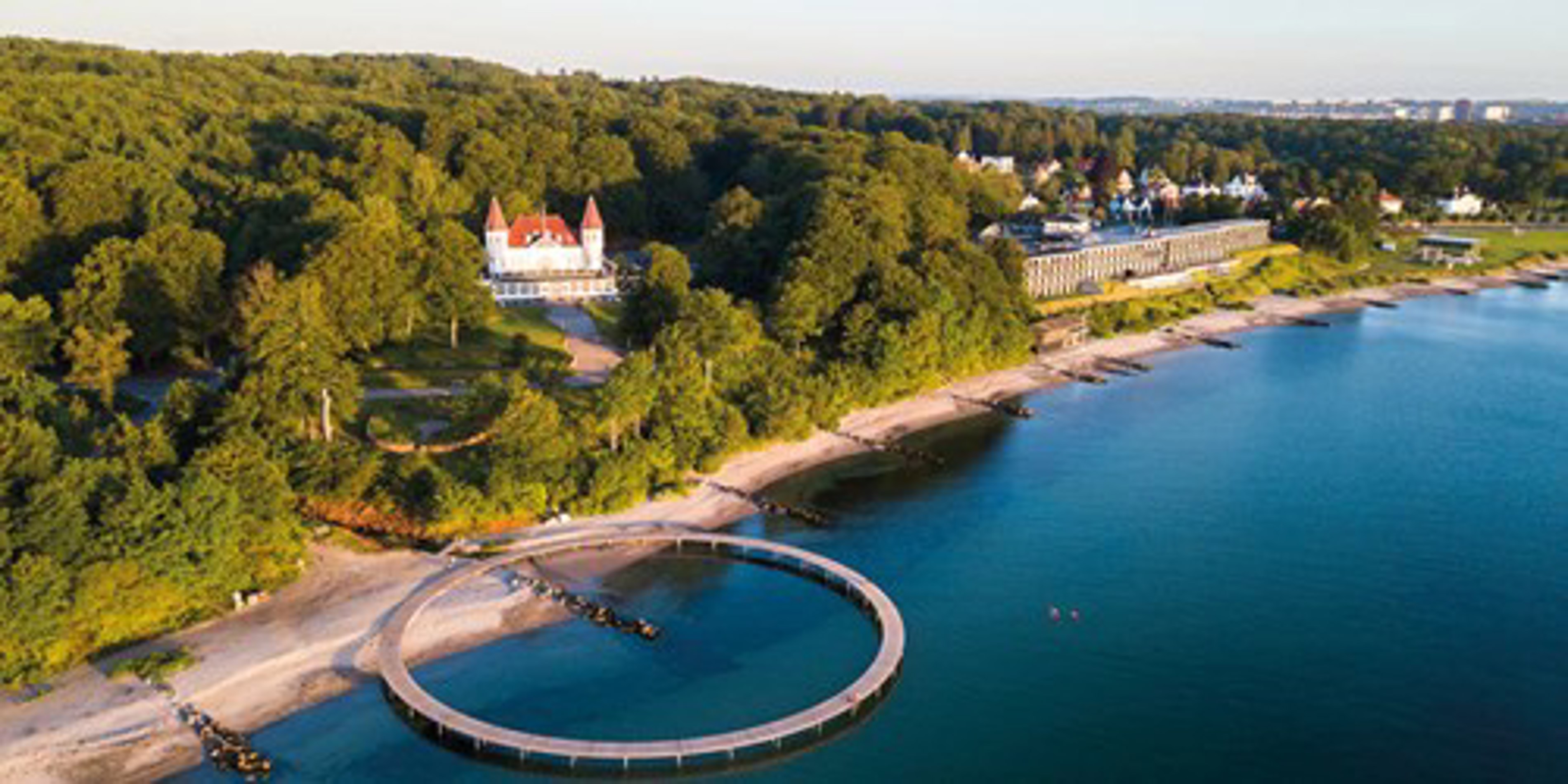 Rund badebro ved Risskov strand med skov og villaer i baggrunden set fra luften.