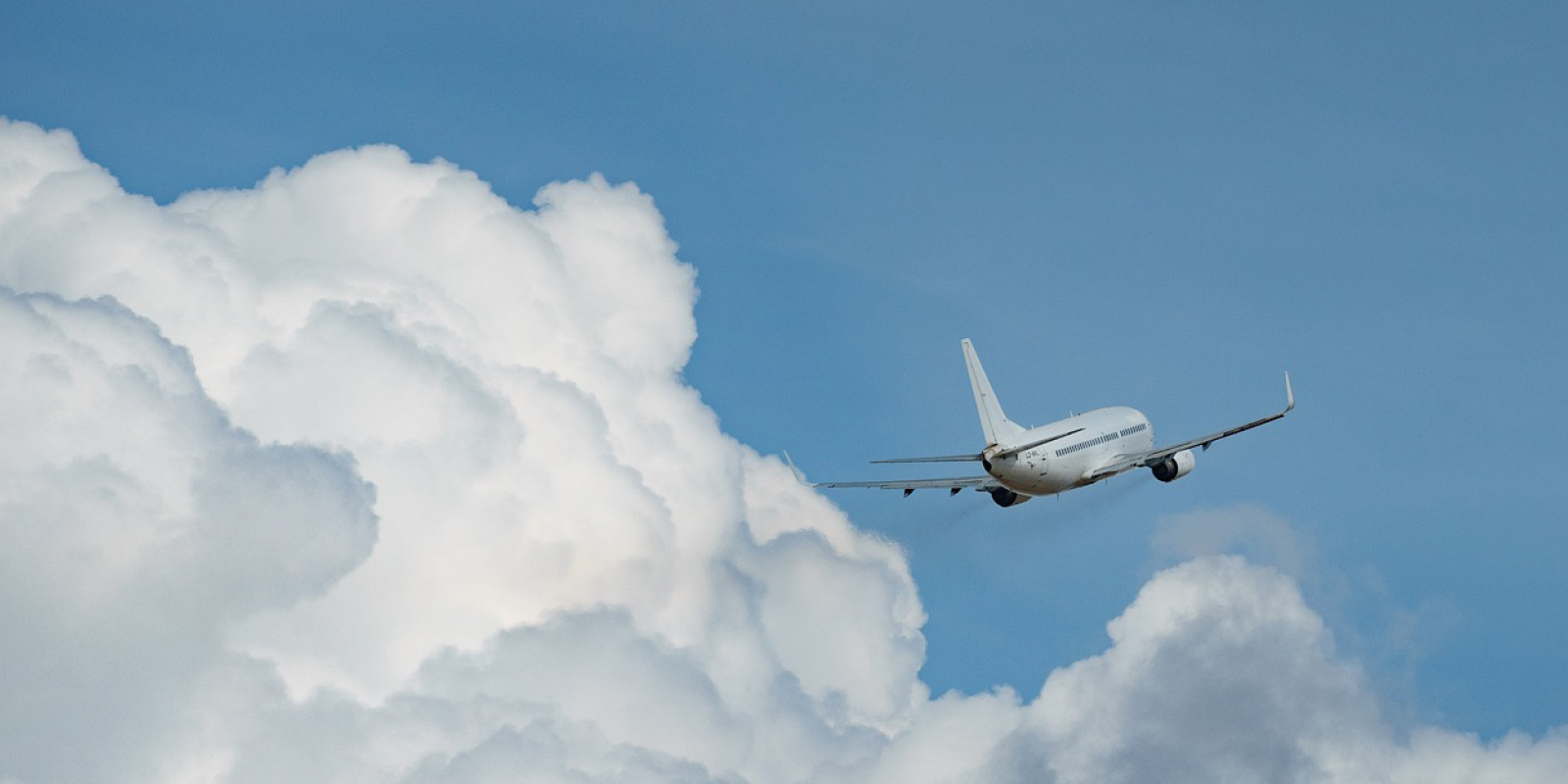 Passagerarflygplan i klart blått himmel ovanför moln fotograferat i vidvinkelperspektiv.