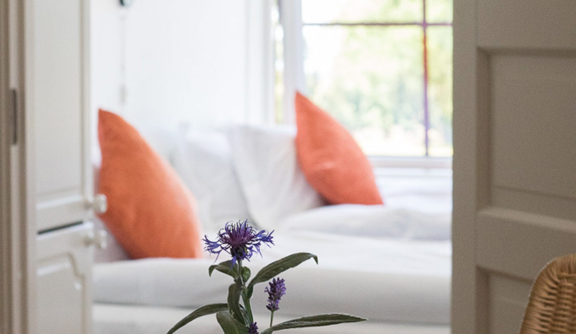 Blomstrende plante på bord i lys soveværelse med orange puder.