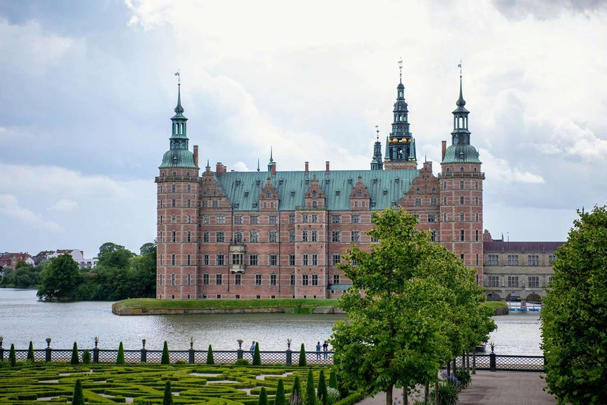 Frederiksborg i solsken omgiven av spegelblankt vatten.