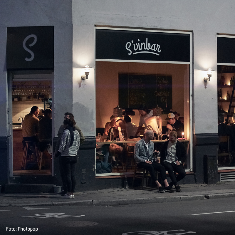 Folk nyder deres aften på Svinbar med hyggelig belysning, mens de sidder ved borde og drikker vin.