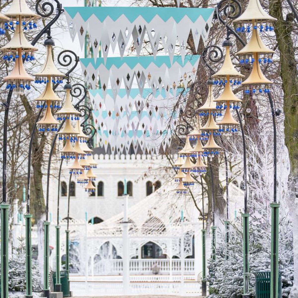 Vinterlys i Tivoli Hovedalleen med elegant belysning och vinterdekorationer i ett snöklätt landskap.