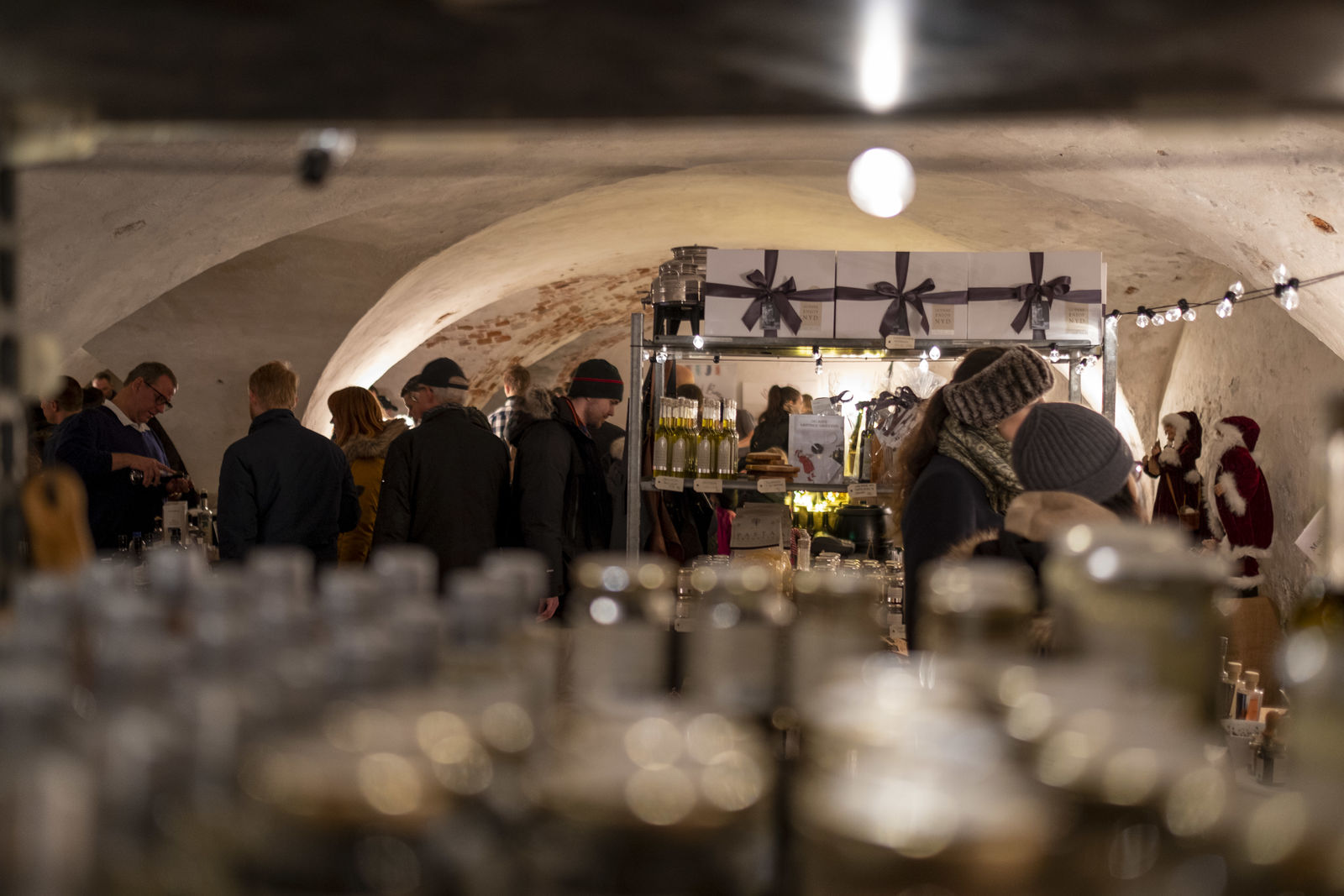 Folk besøger en julemarkedstand med håndlavede varer i en kælder med hvælvede lofter.