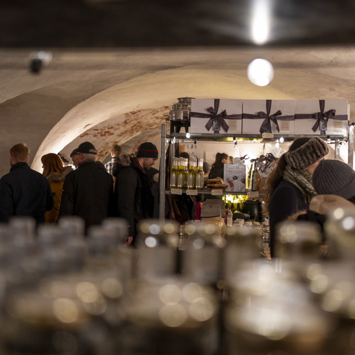 Folk besøger en julemarkedstand med håndlavede varer i en kælder med hvælvede lofter.