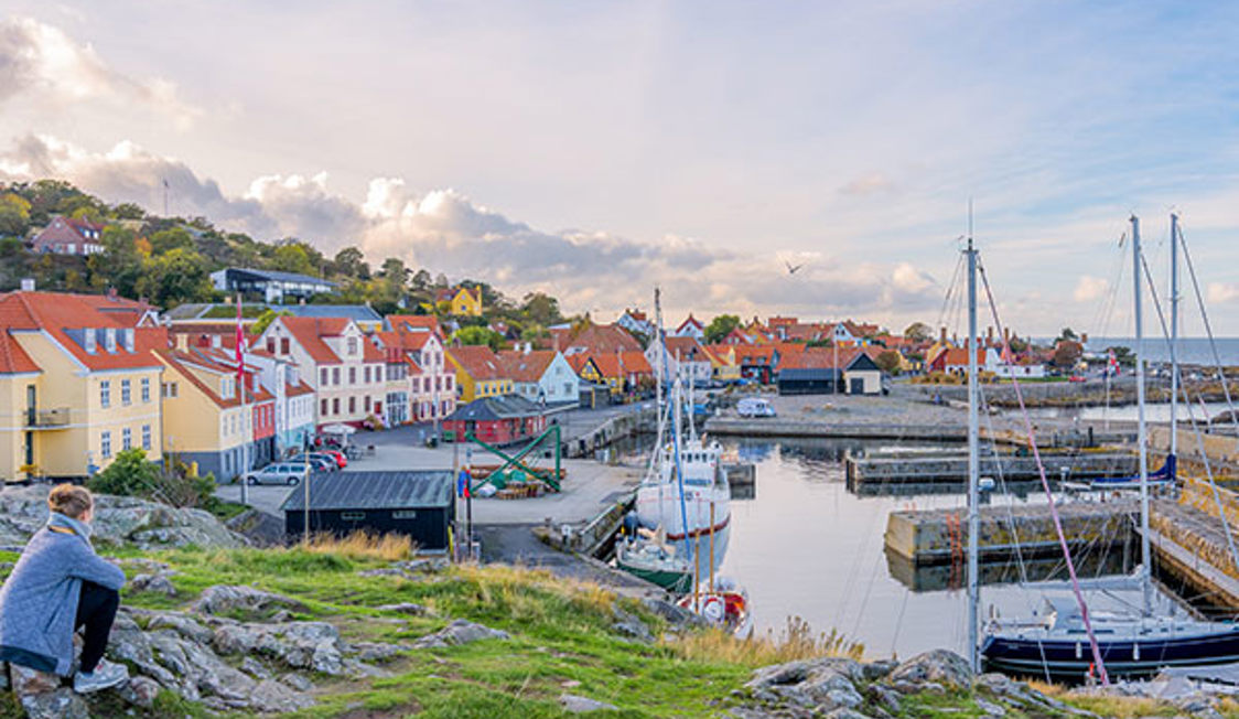 Udsigt over Allinge havn med sejlbåde og farverige huse i solrigt vejr på Bornholm.
