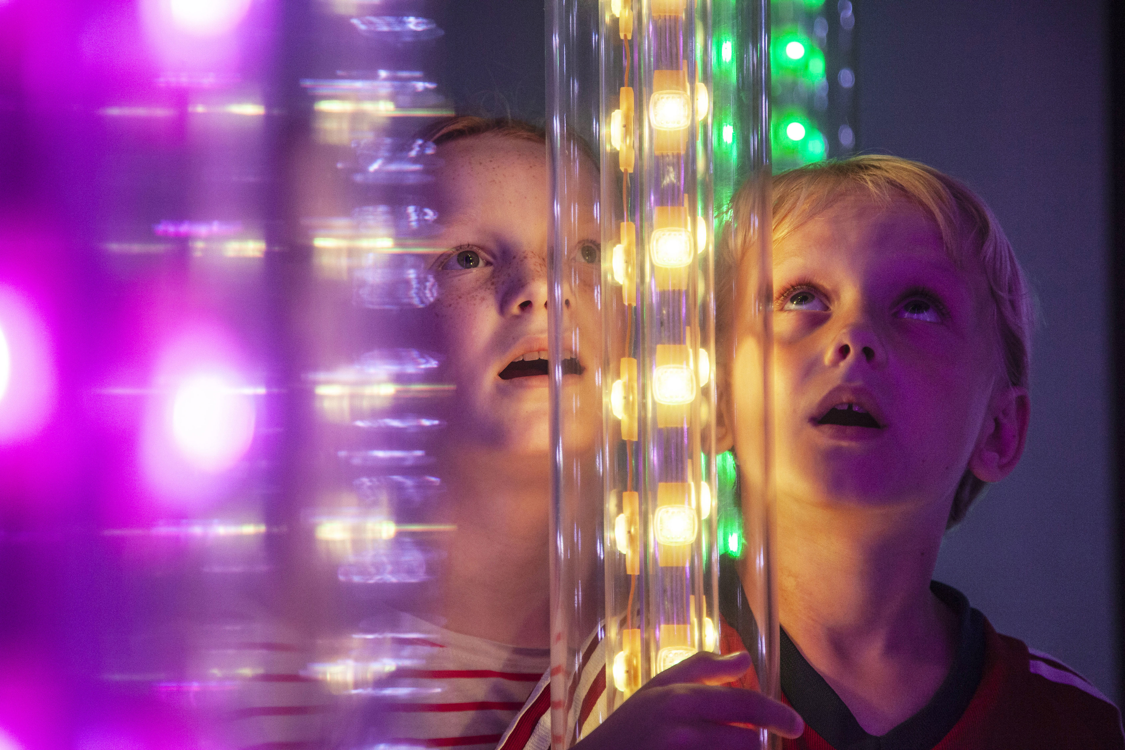 Två barn tittar fascinerat på lysande installationen Lyslabyrinten 5 med färgglada lampor.