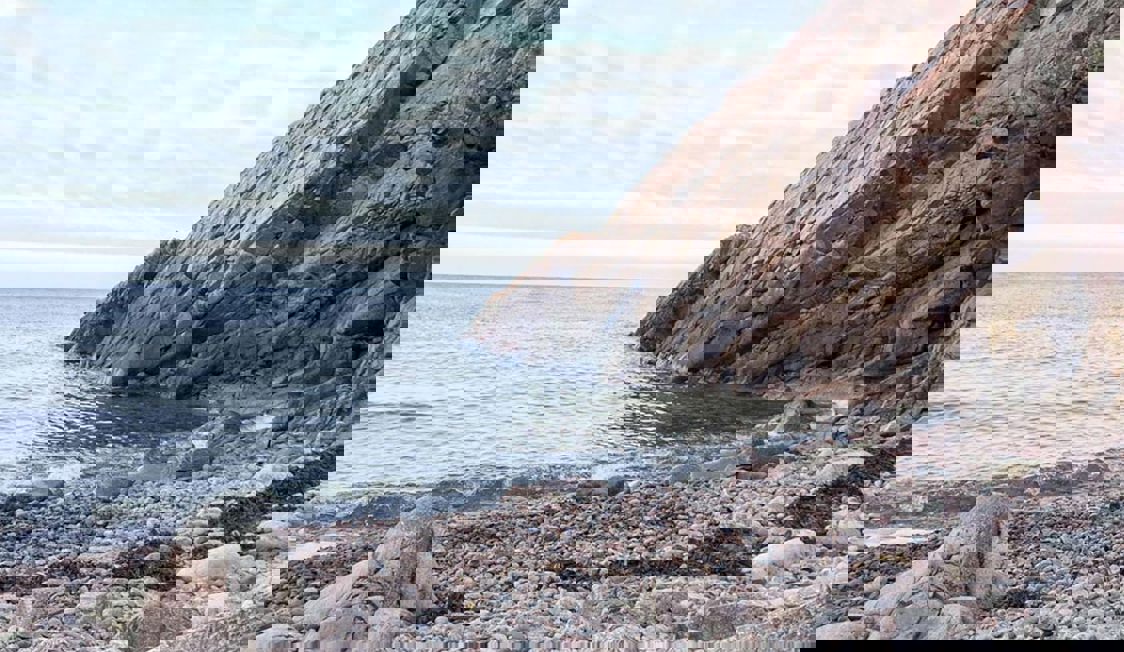 Sejlbåd navigerer gennem klart, blåt hav mellem klippeformationer i et naturbillede i fugleperspektiv.