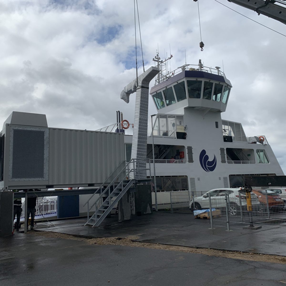 Færge ved kaj med bro til boarding og skibets kommandotårn synligt under en skyet himmel.