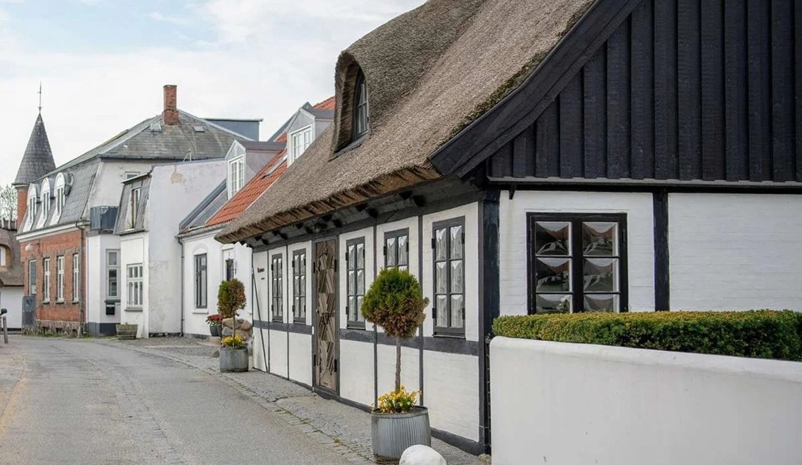 Traditionellt korsvirkeshus i Gilleleje med halmtak och vita väggar, längs en pittoresk gata.