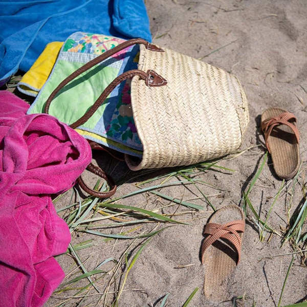 Strandväska från Danska Rivieran Nordsjälland i sanden med färgglada handdukar och sandaler.