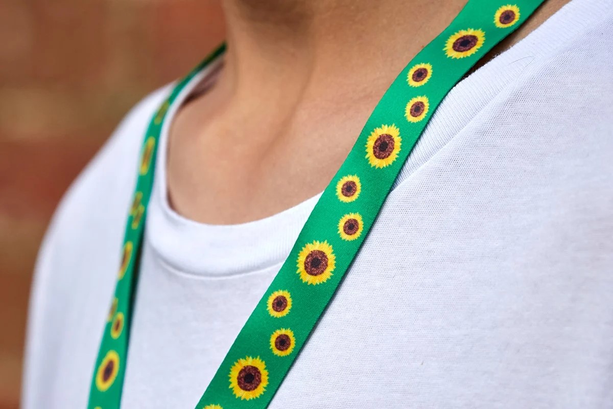 Grön nyckelband med solrosmönster bärs över en vit tröja.