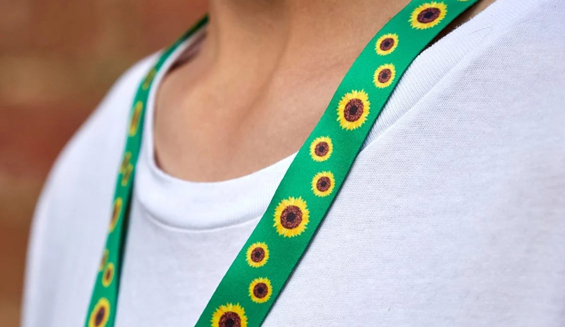 Grøn nøglesnor med solsikkeprint bæres over en hvid trøje.