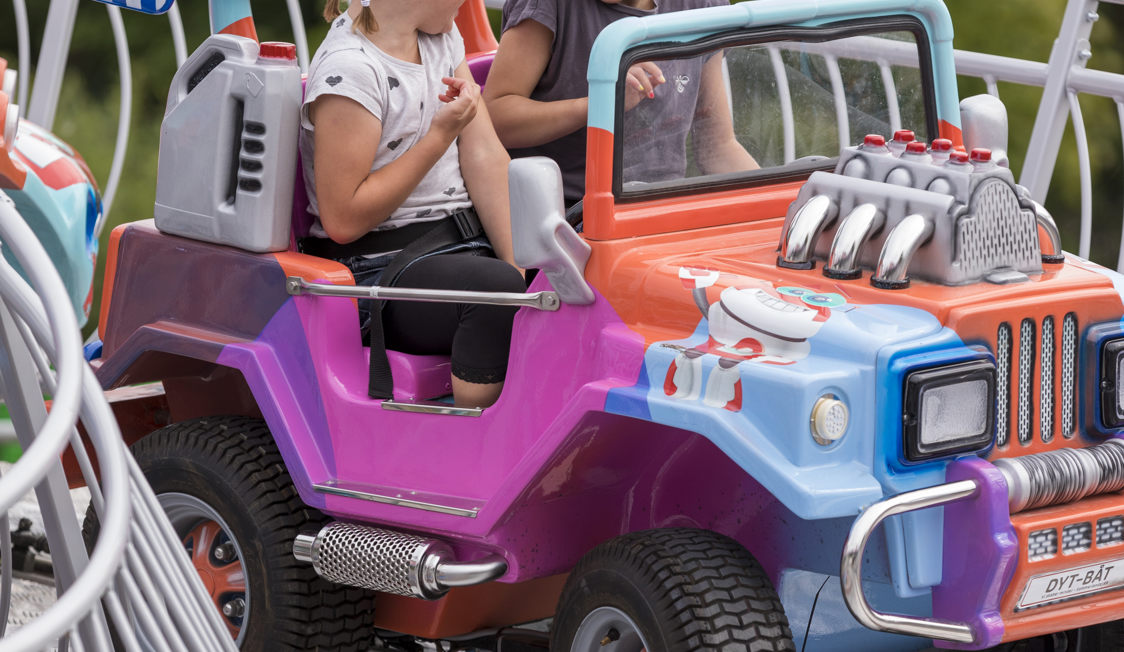 Två barn åker en färgglad karusellbil med SS 2802 2 i en nöjespark.