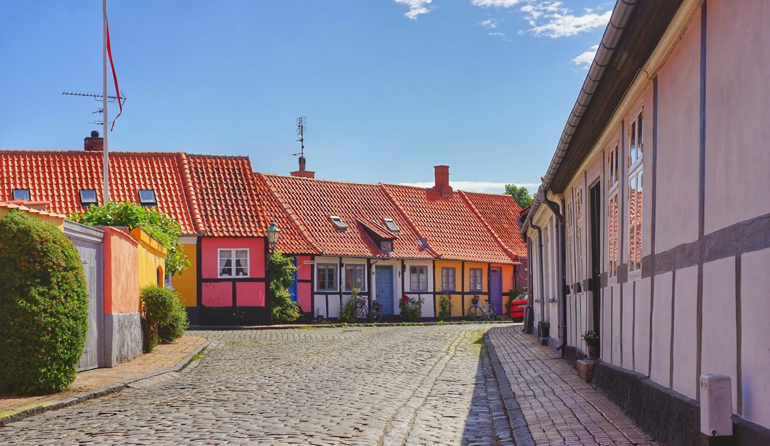 Traditional colorful houses along a cobblestone street under a clear blue sky in a cozy Swedish village.