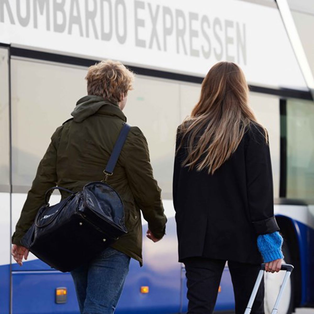To personer går mod Lombardo Expressen med bagage på en busterminal.