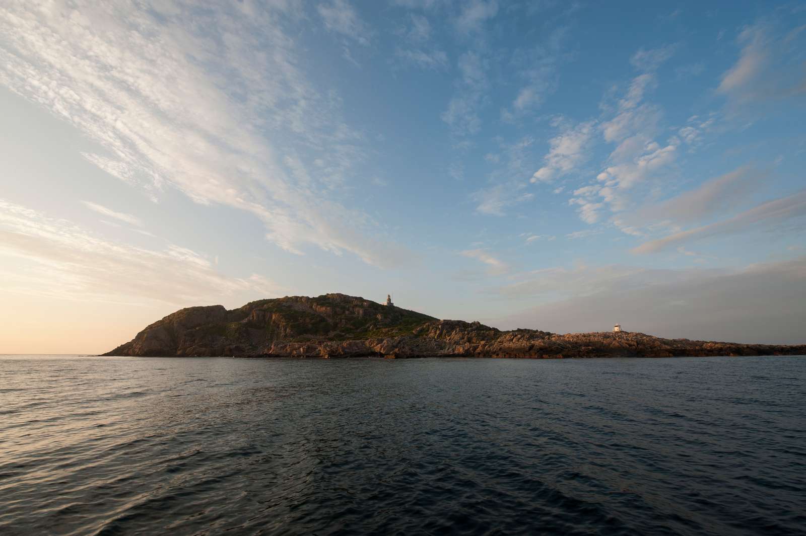 Fyret på en klippeø set fra havet ved solopgang under en klar himmel.