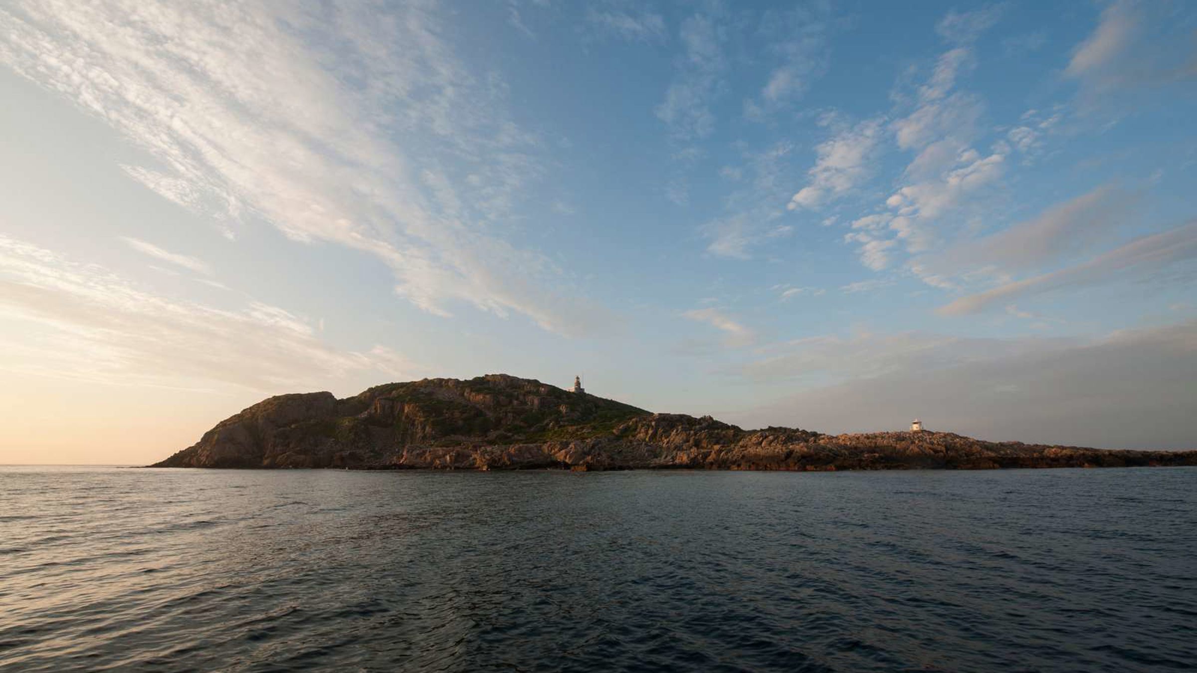 Fyret på en klippeø set fra havet ved solopgang under en klar himmel.