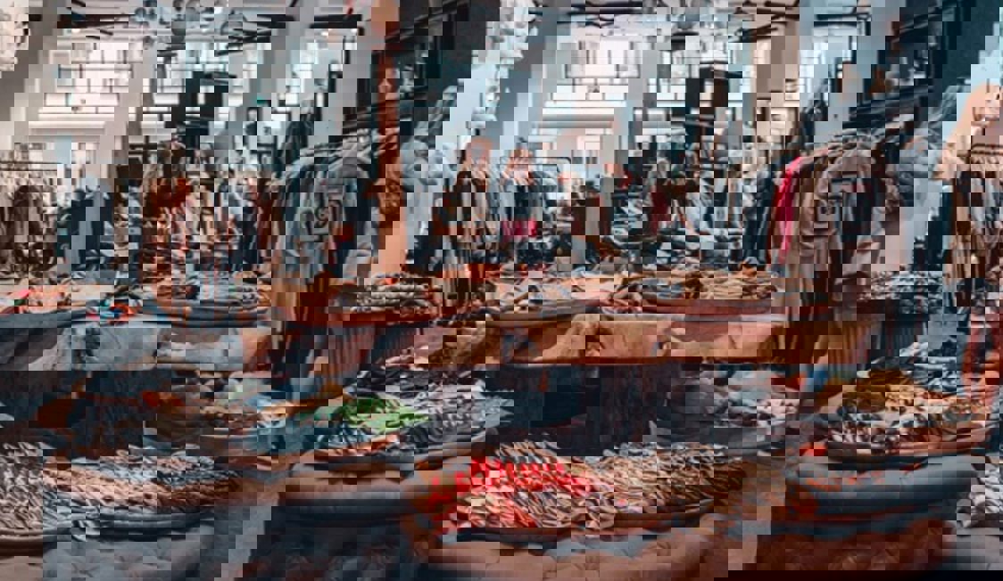 Inne i en butik finns en mängd kläder utställda på bänkar, bord och ställningar.