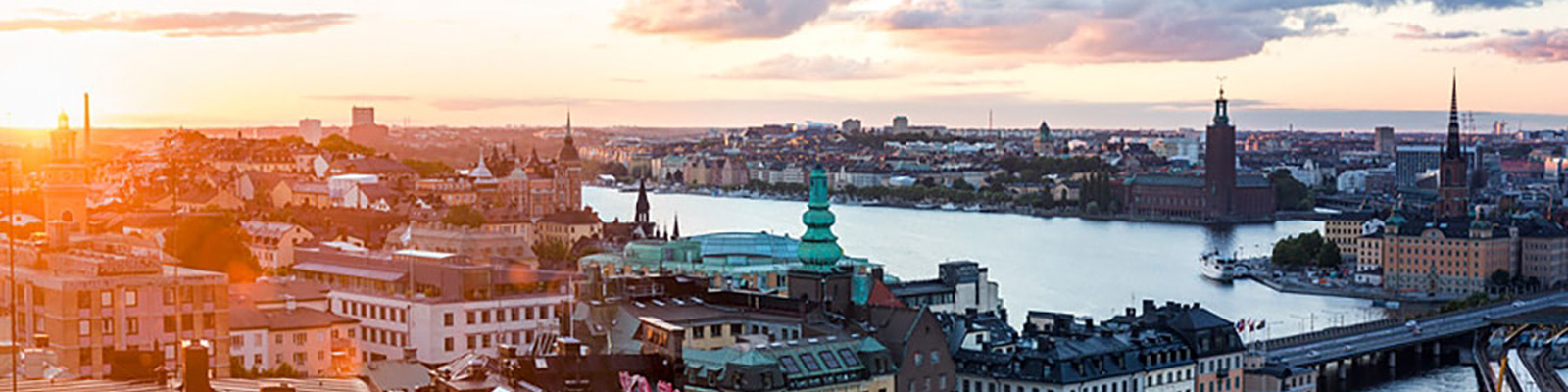 Stockholm by med udsigt over vandet ved solnedgang, med historisk arkitektur og kirketårne i horisonten.