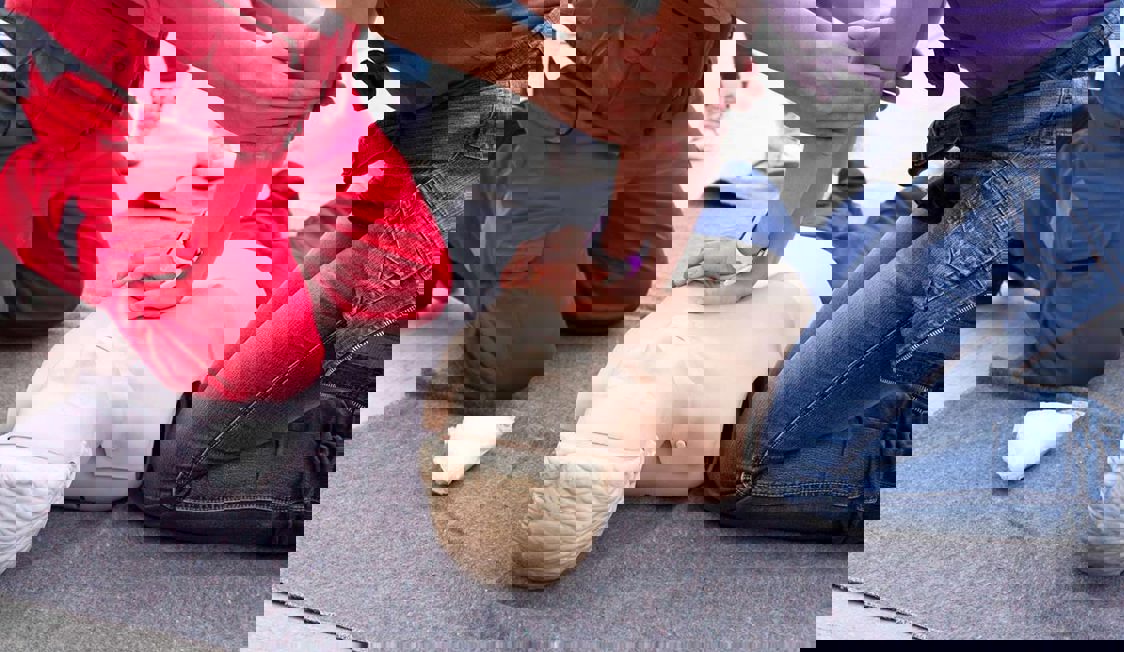 En kvinna lär sig första hjälpen av en man i röd uniform i en utbildningssession.