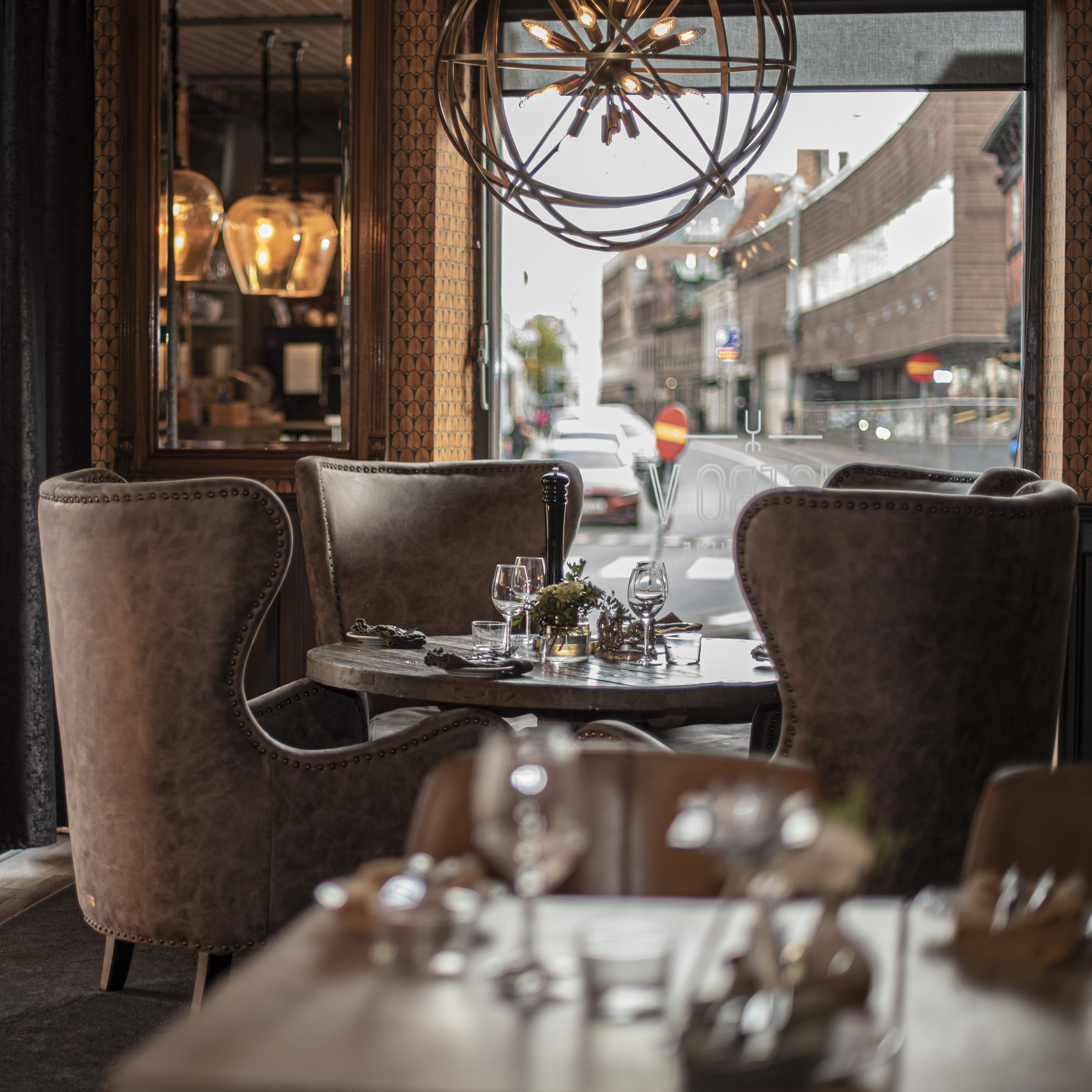 Eksklusivt spisebord med dækket service og lænestole i en hyggelig restaurant nær vinduet med gadekig.
